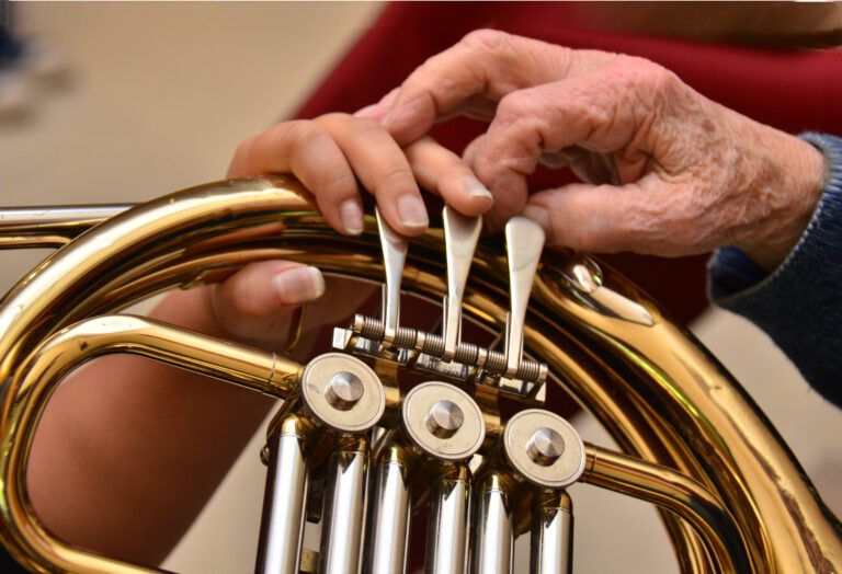 older hand guides younger hand in playing the french horn