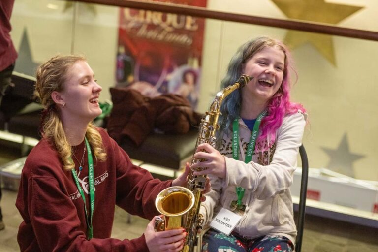 young girl learns how to play the saxophone at family discovery concert for all ages