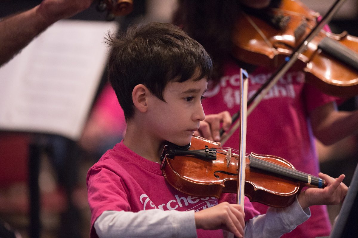 young boy plays violin in orchestra rouh