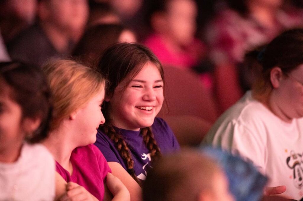 young girl laughs with friend in concert hall at family discovery concert for all ages