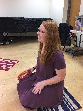 woman with long hair and glasses smiles as she plays the tamborine