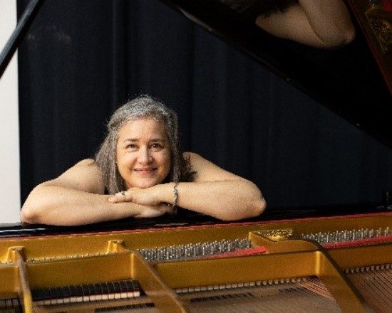 woman with short hair leans on a piano