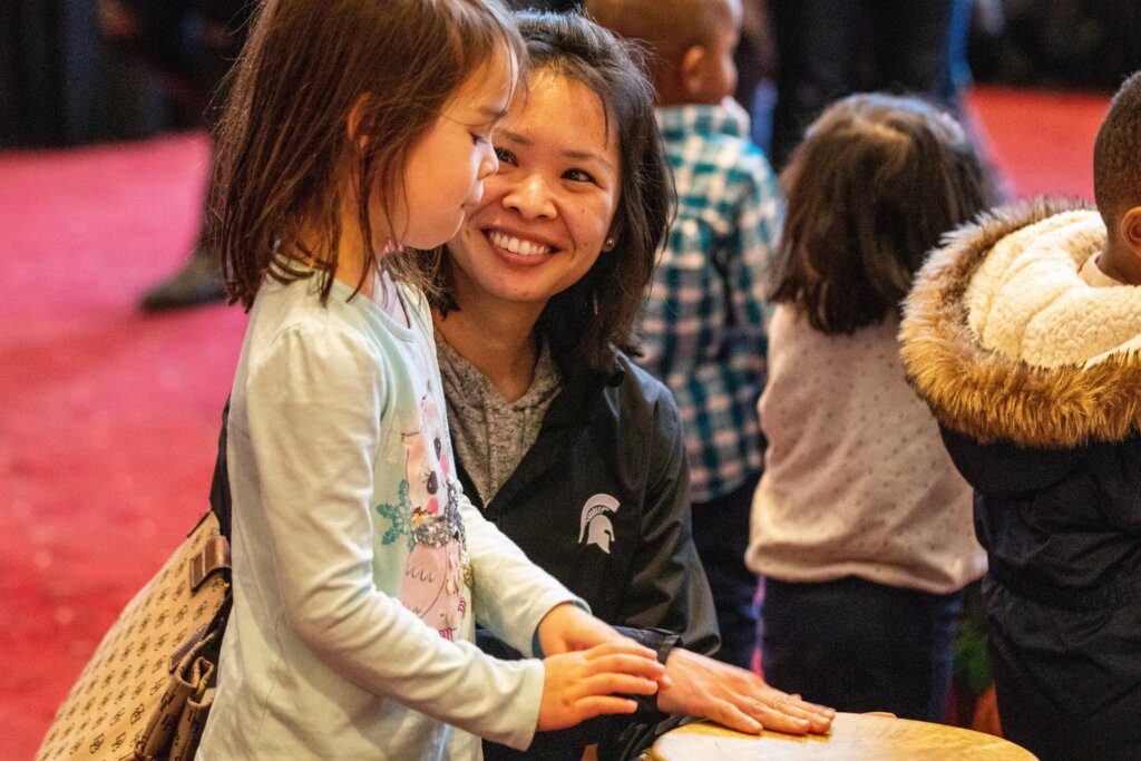mom watches as daughter learns to play drums at family discovery concert for all ages